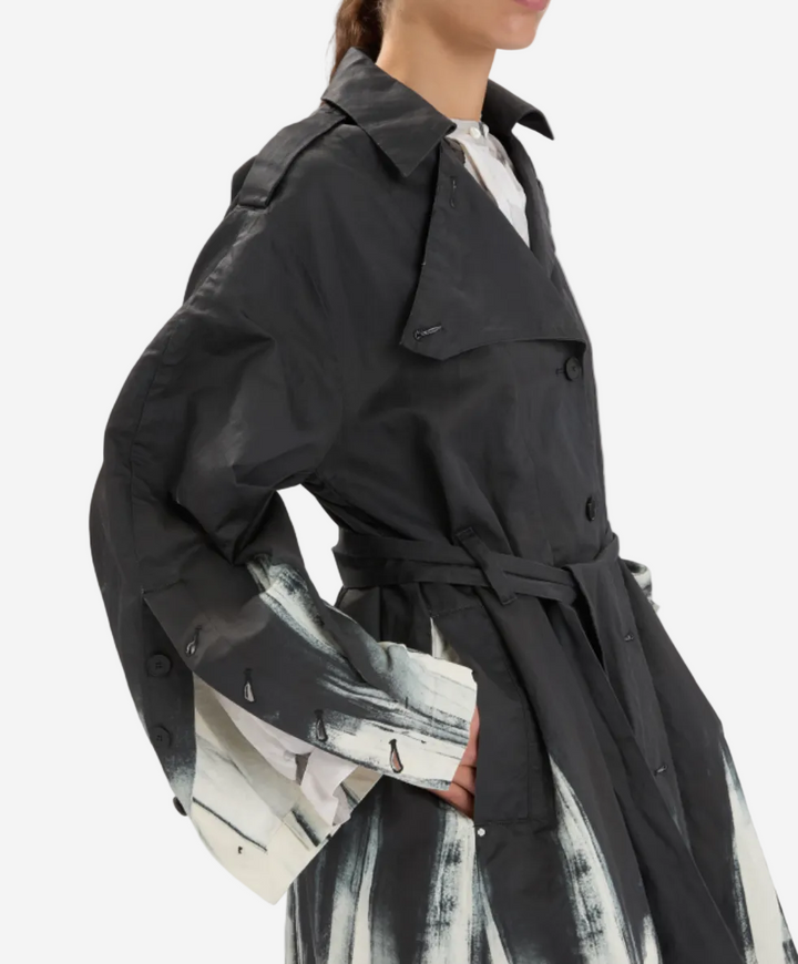 Person wearing a black trench coat over a patterned dress on a white background