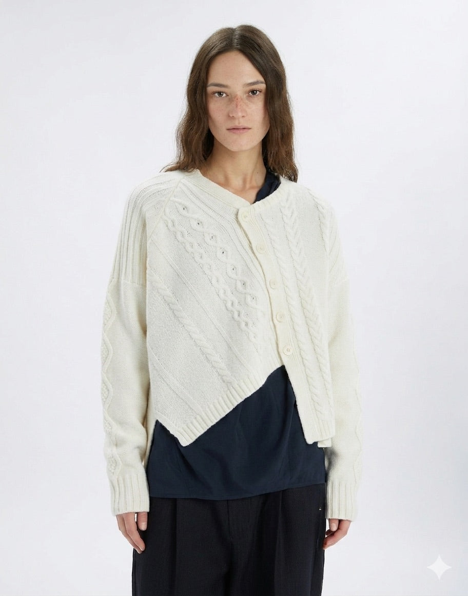 Woman wearing a cream-colored cable knit cardigan over a navy shirt on a white background