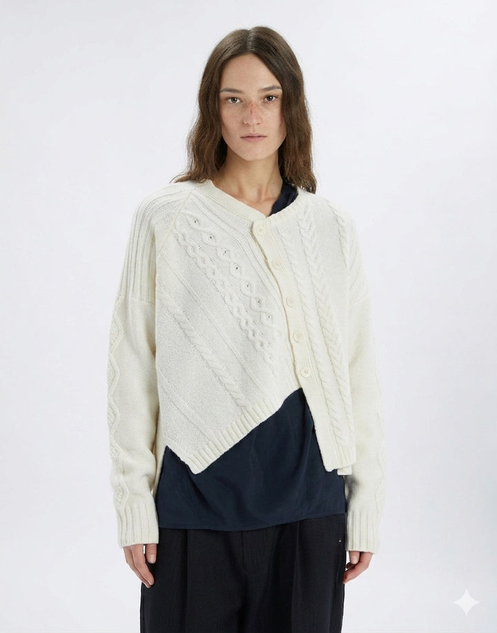 Woman wearing a cream-colored cable knit cardigan over a navy shirt on a white background