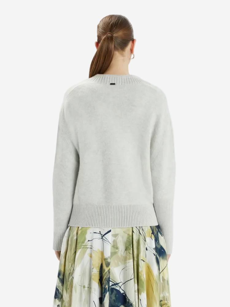 Person wearing a light gray sweater and floral skirt on a white background