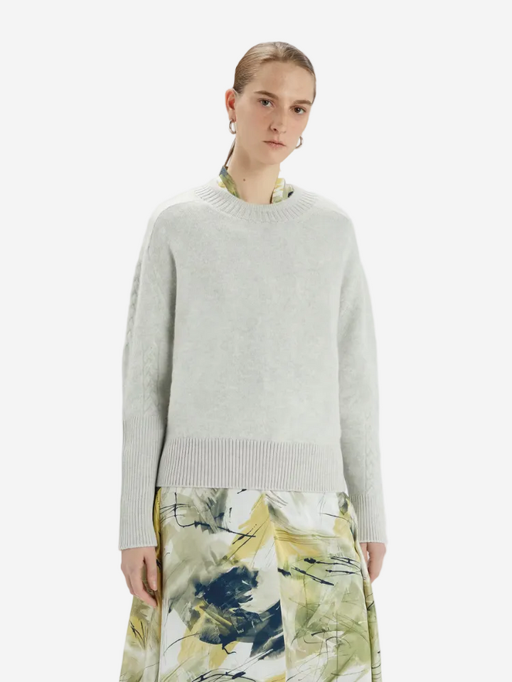 Person wearing a light gray sweater over a patterned skirt on a white background