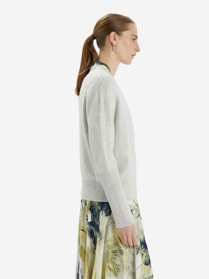 Woman wearing a light gray sweater and floral skirt on a white background