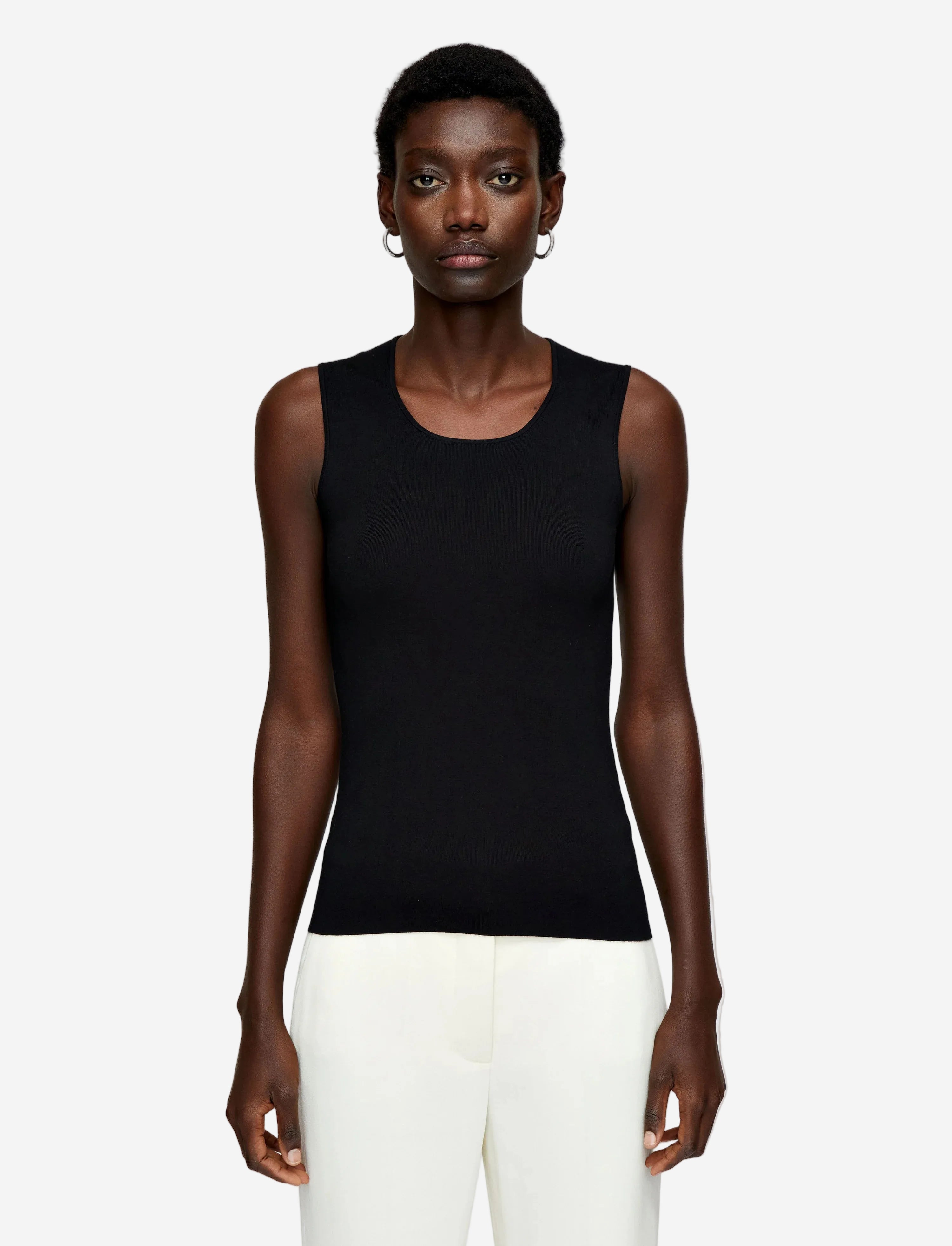 Person wearing a black sleeveless top and white pants on a plain background