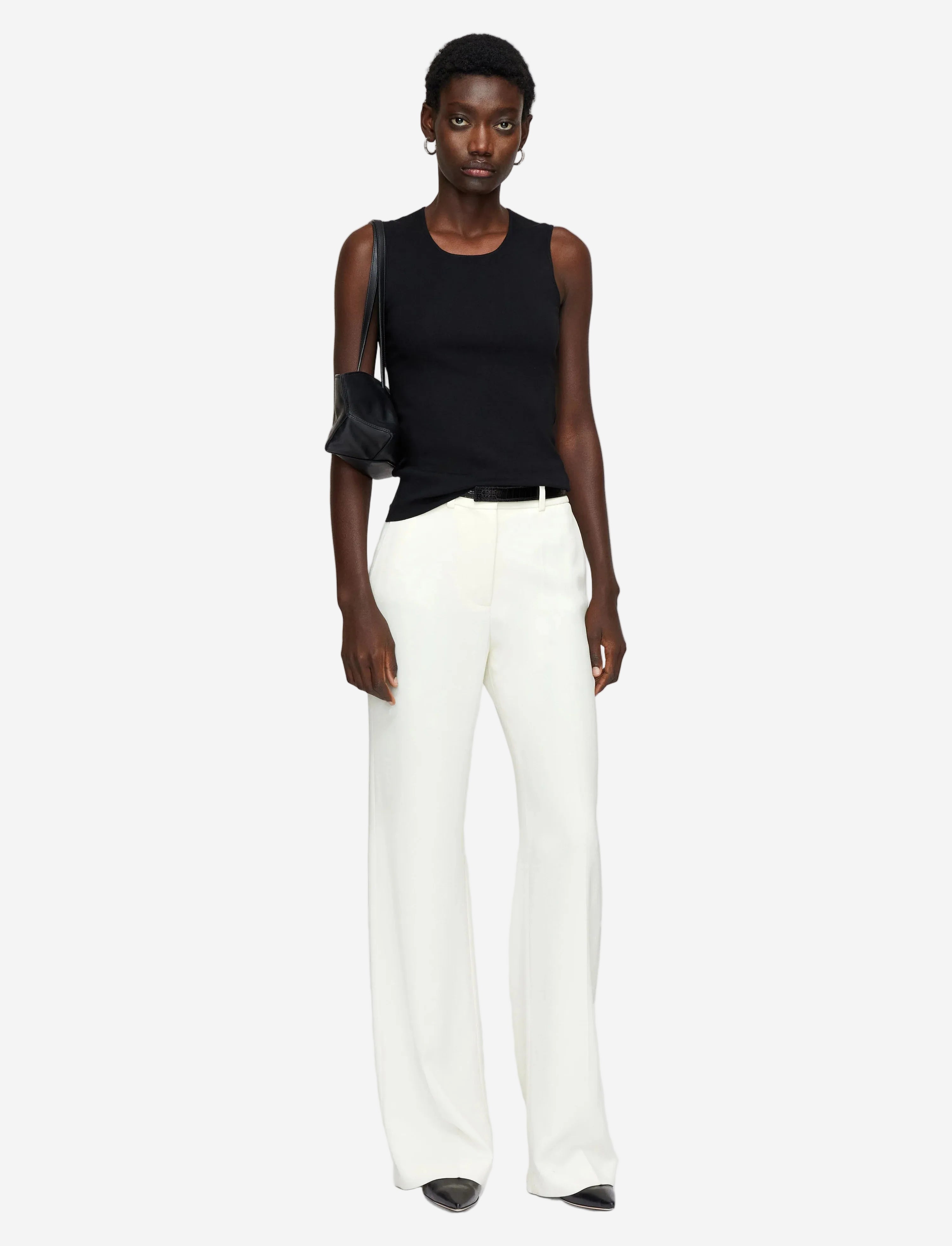 Person wearing a black sleeveless top and white pants on a plain background