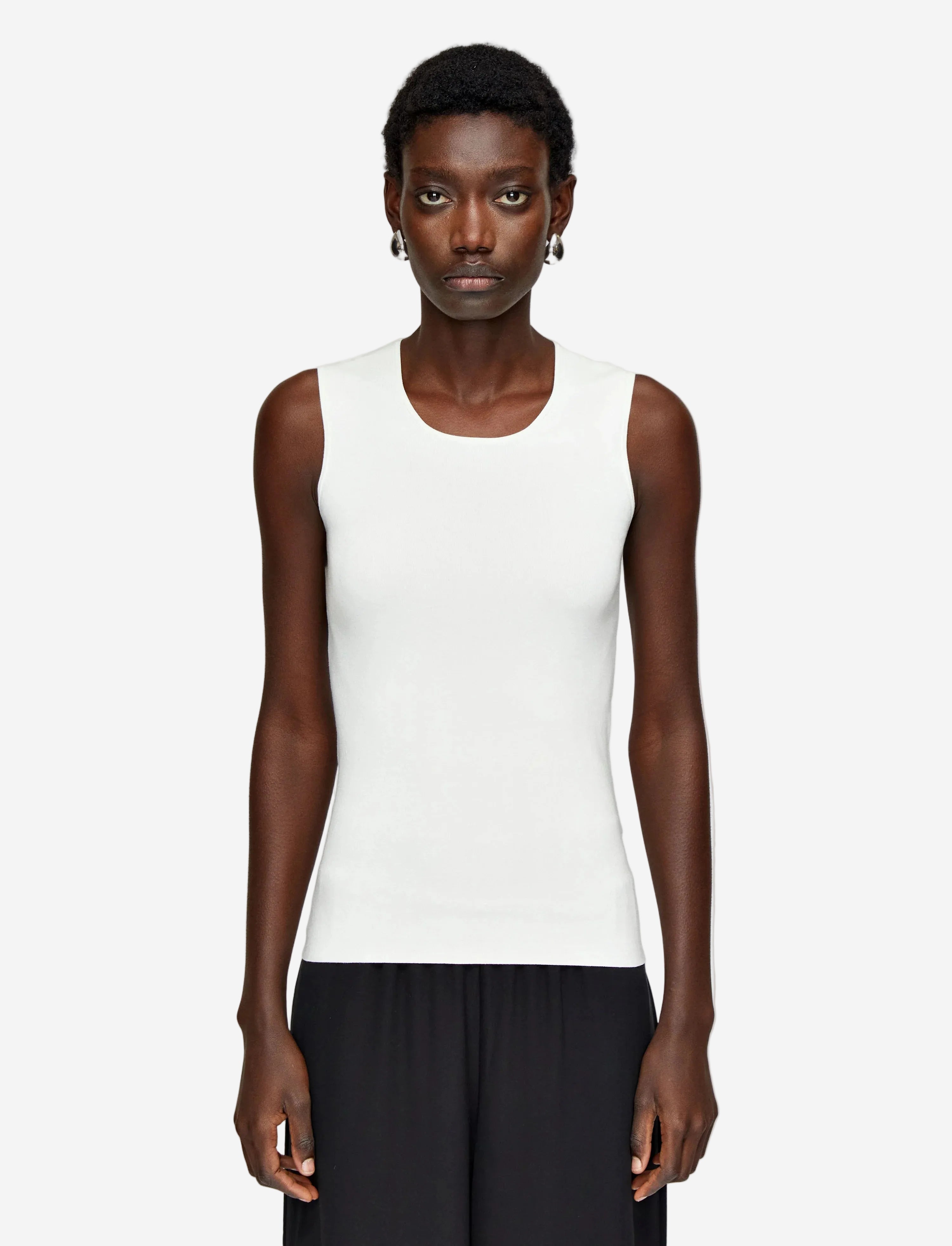 Person wearing a white sleeveless top and black pants on a light gray background