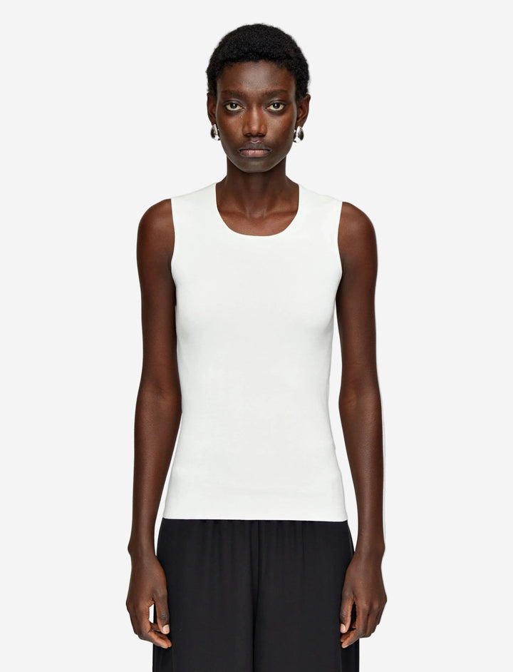 Person wearing a white sleeveless top and black pants on a light gray background