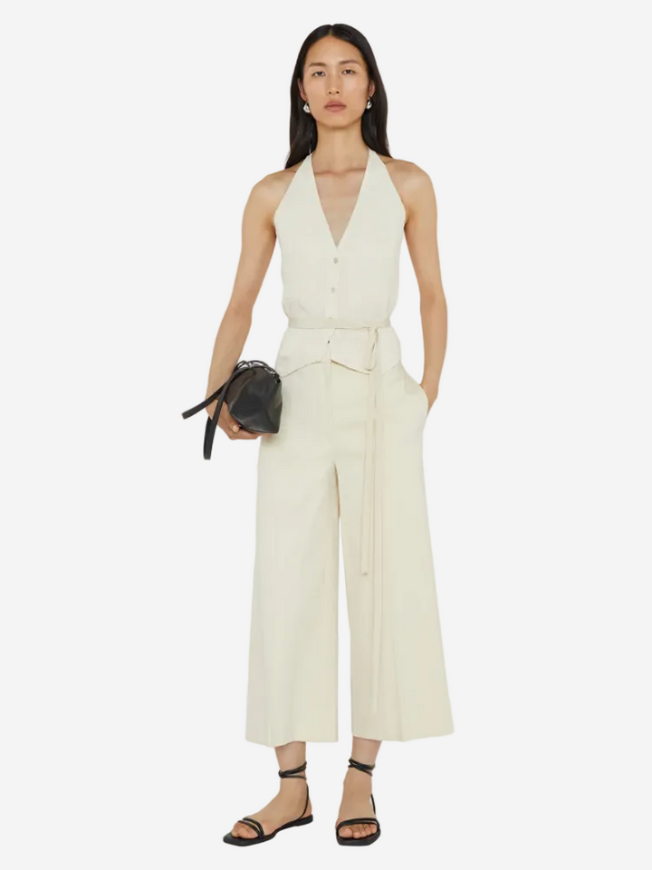 Woman wearing a white jumpsuit holding a black handbag on a white background
