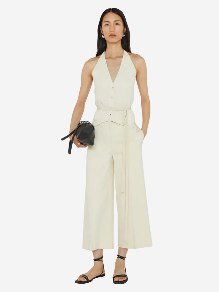 Woman wearing a white jumpsuit holding a black handbag on a white background