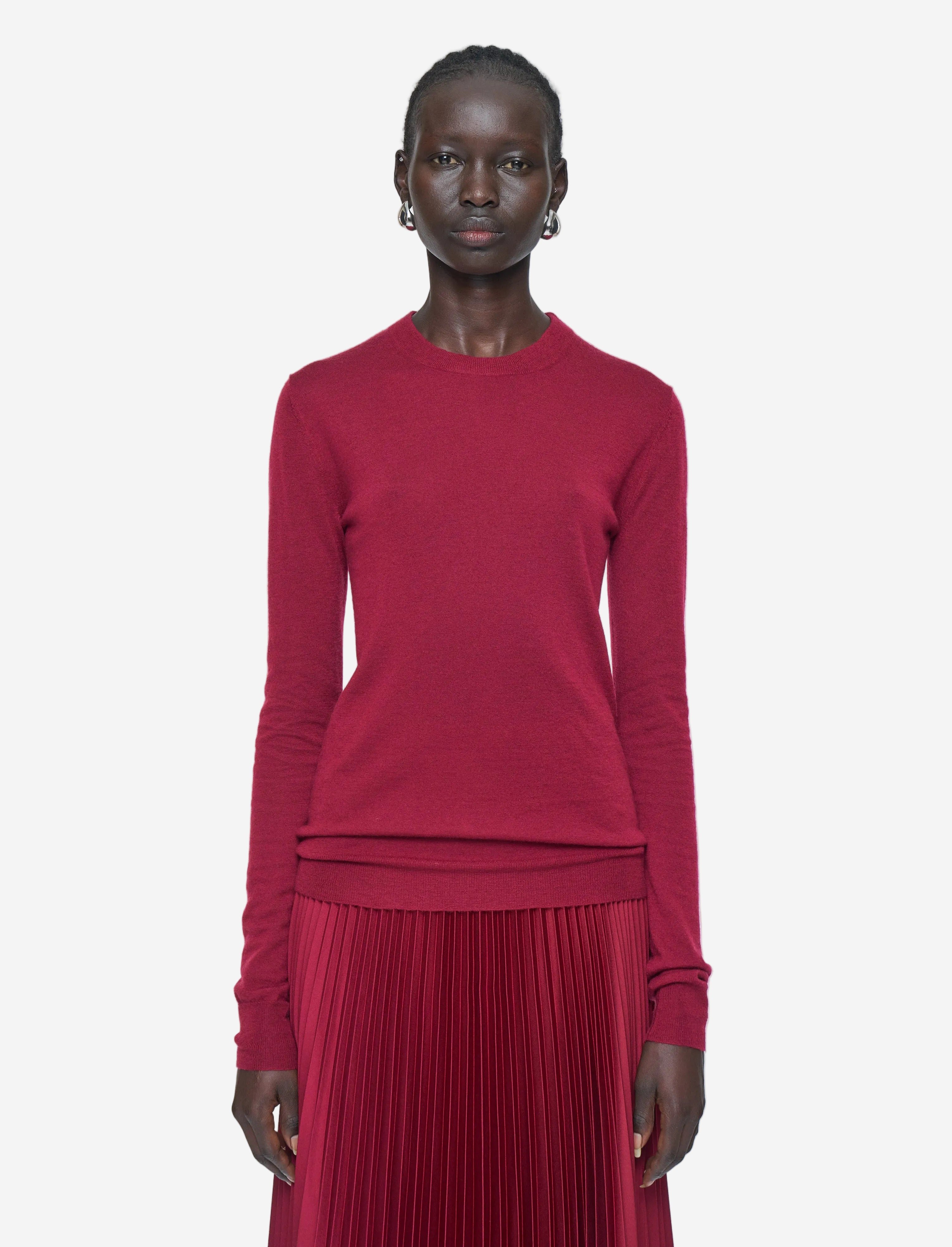 Person wearing a red sweater and pleated skirt on a white background