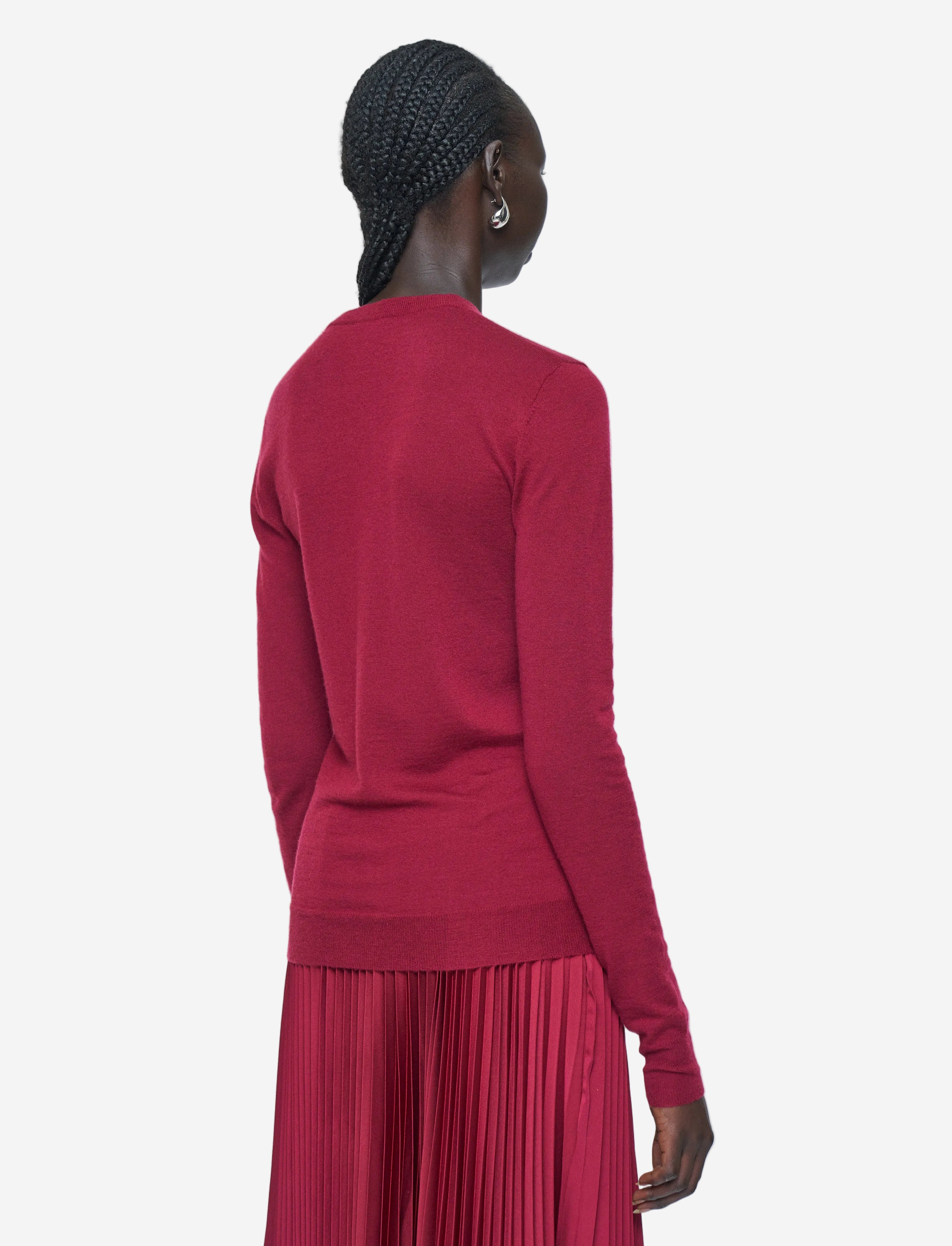 Person wearing a red long-sleeve top and pleated skirt on a white background