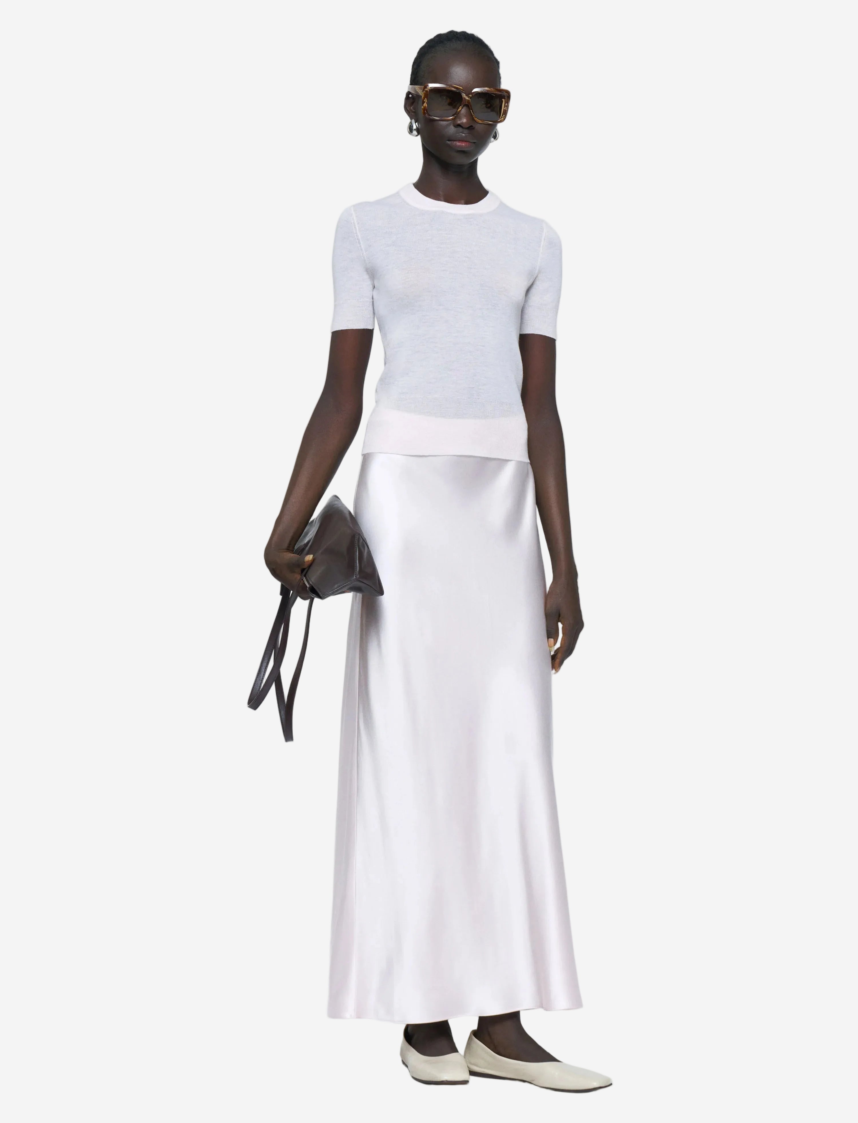 Person wearing a white top and white skirt with a black handbag on a light gray background