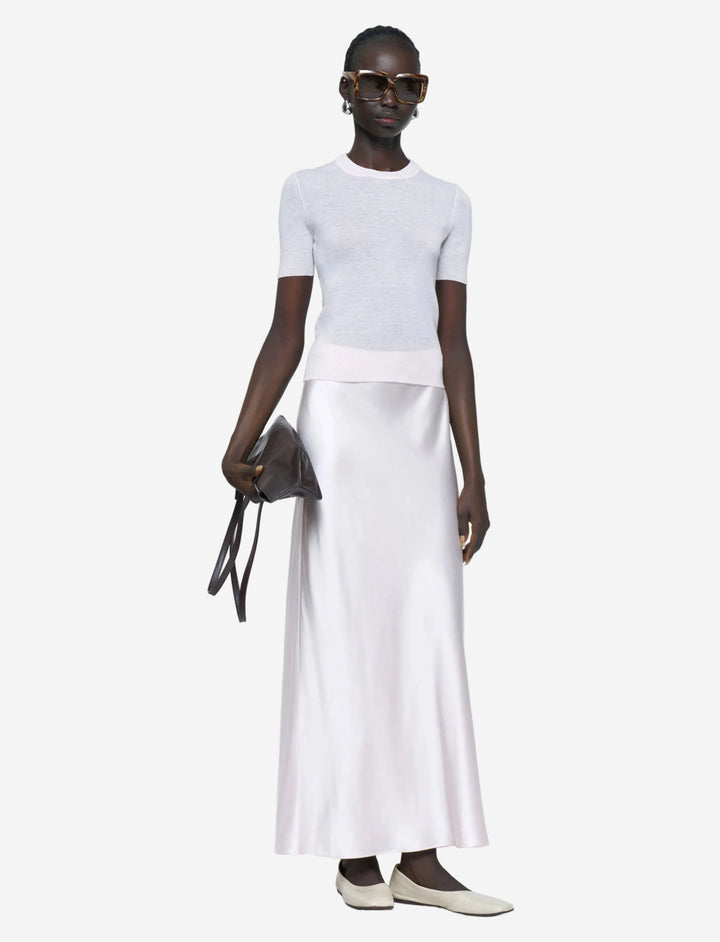 Person wearing a white top and white skirt with a black handbag on a light gray background