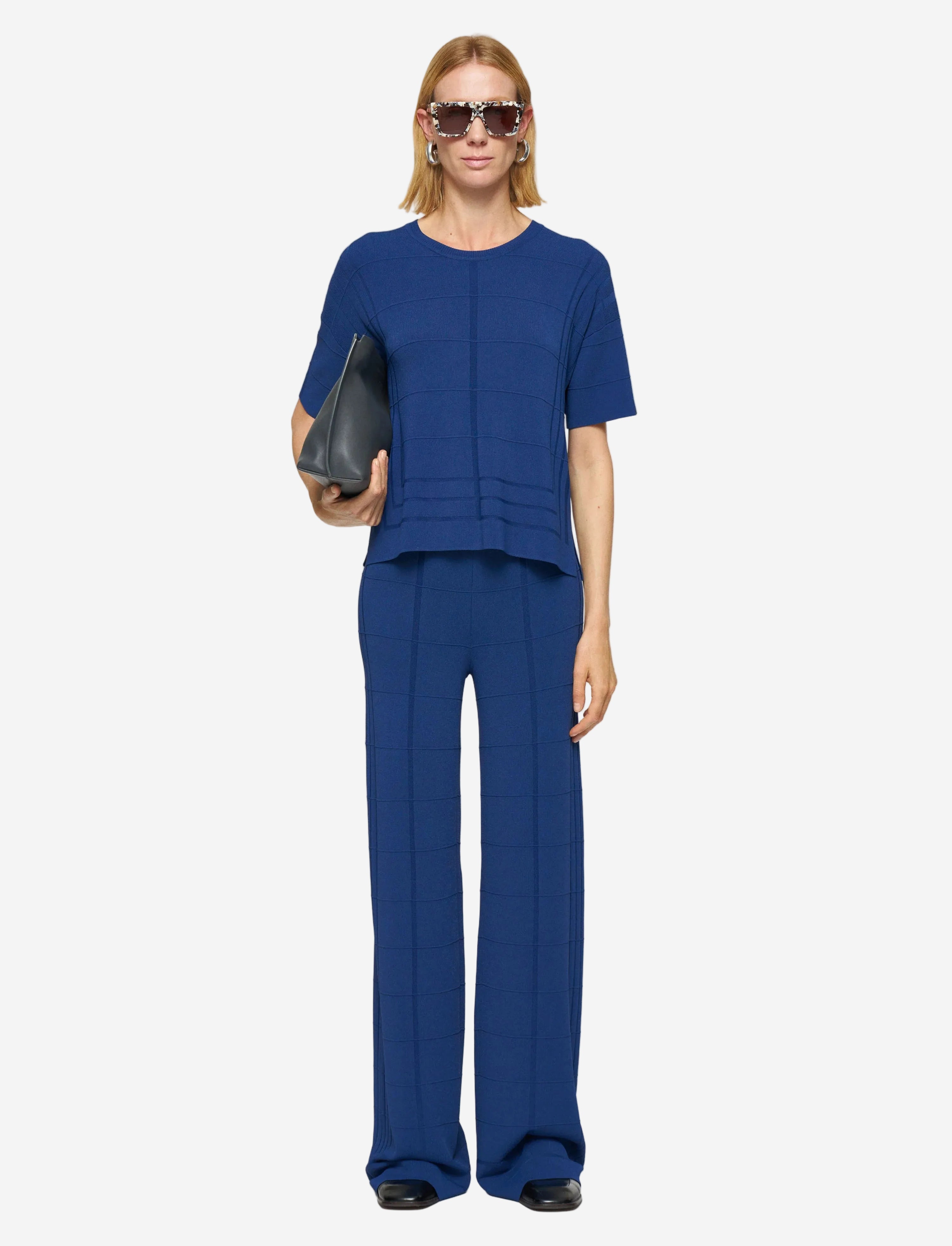 Woman wearing a blue outfit holding a black clutch against a white background
