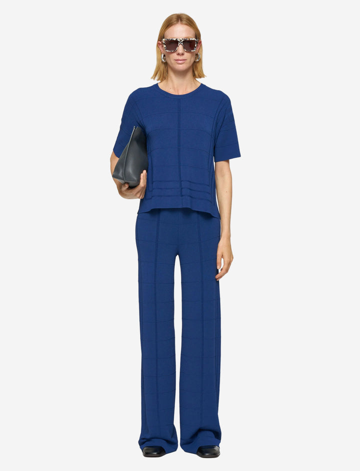 Woman wearing a blue outfit holding a black clutch against a white background