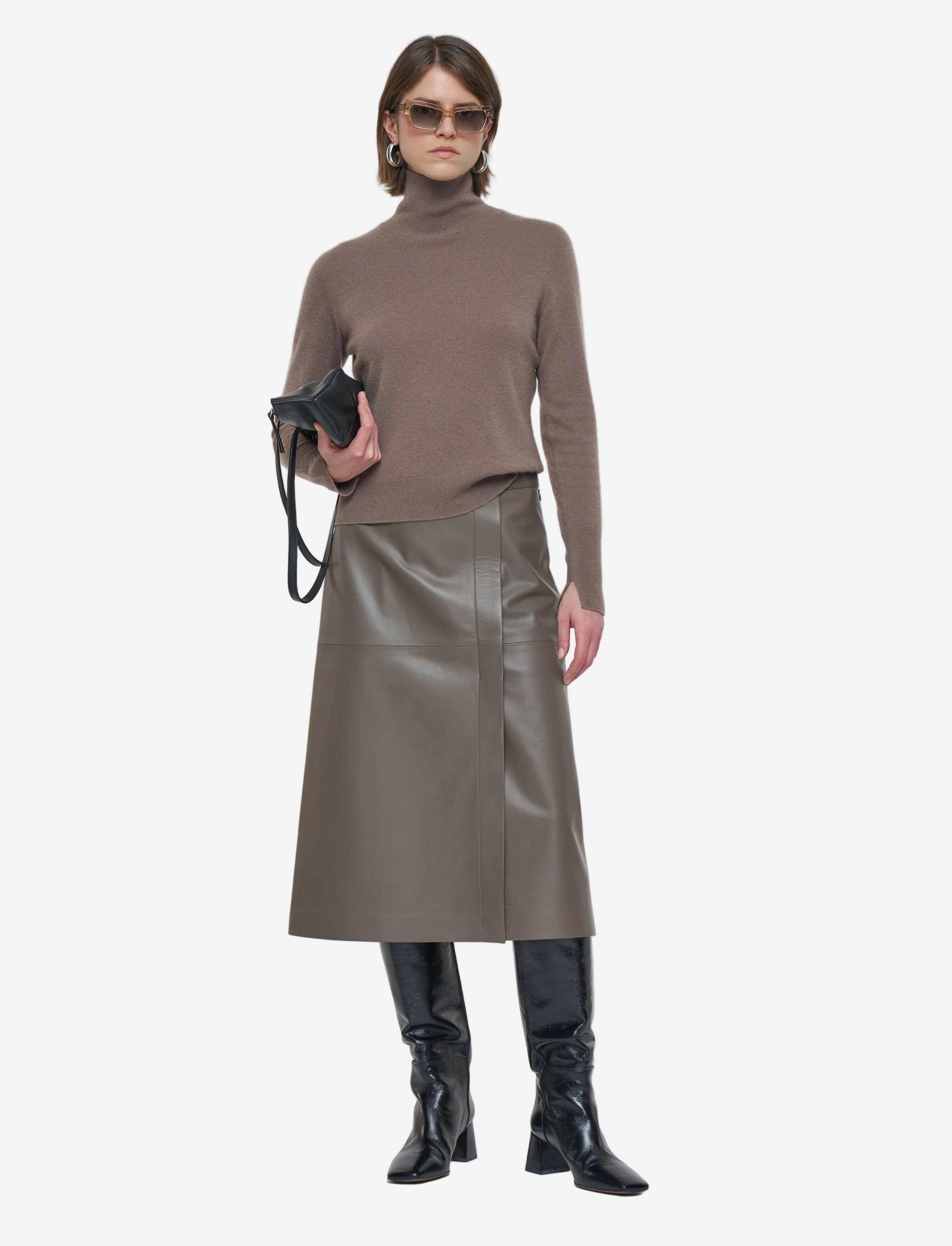 Woman wearing a brown turtleneck, leather skirt, and black boots on a white background