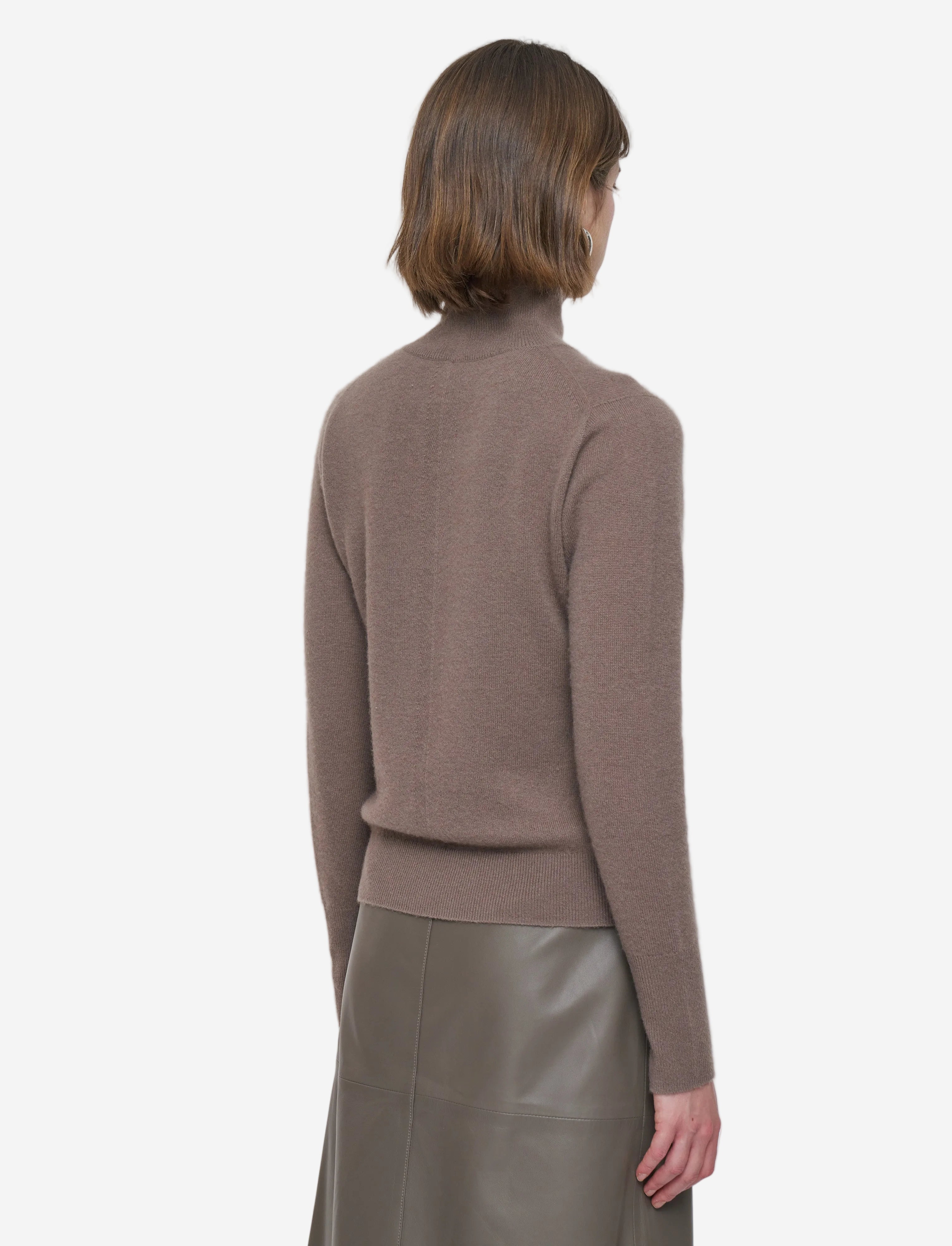Close-up of a person wearing a brown turtleneck sweater with hoop earrings.