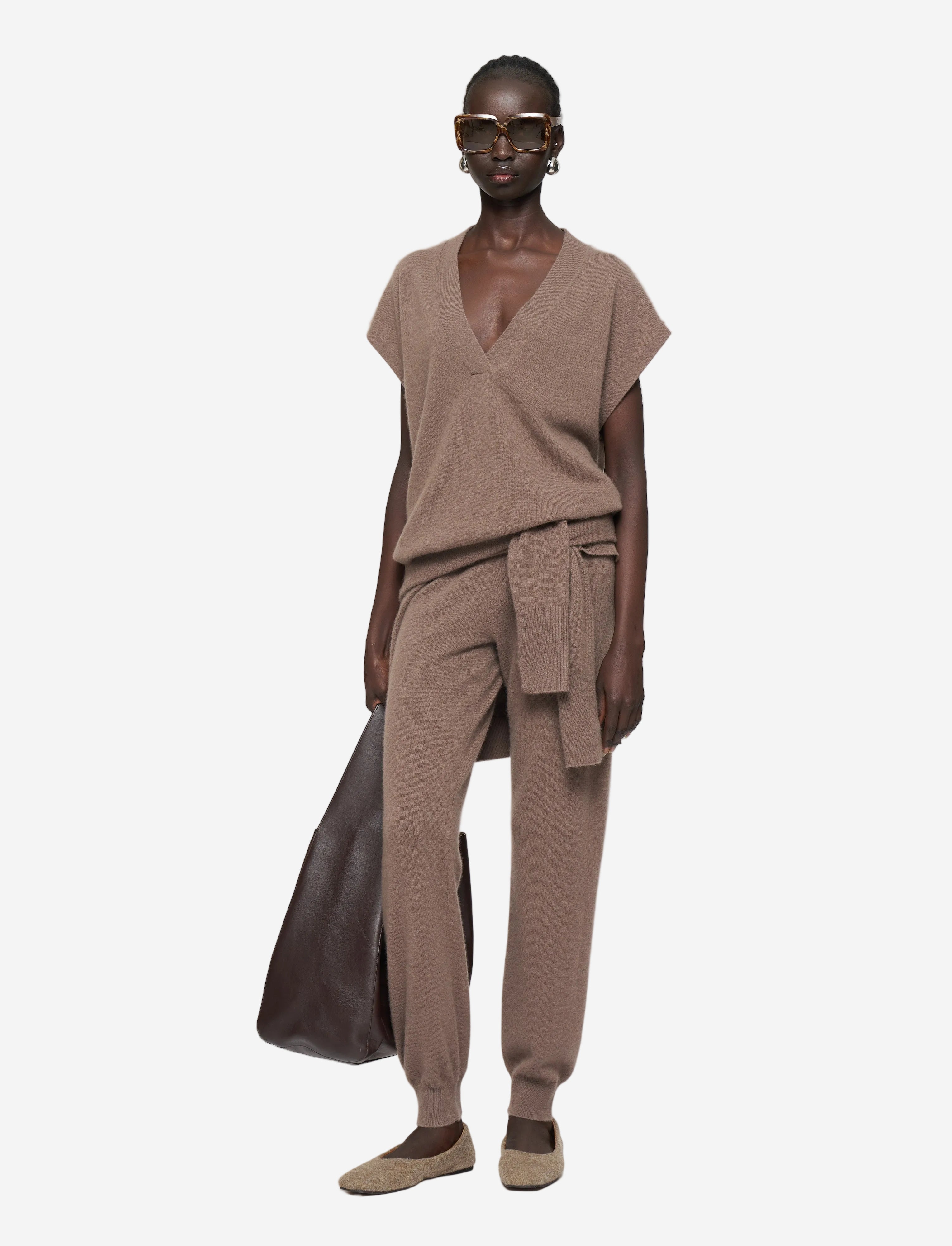 Person wearing a brown outfit with a draped top and pants on a white background