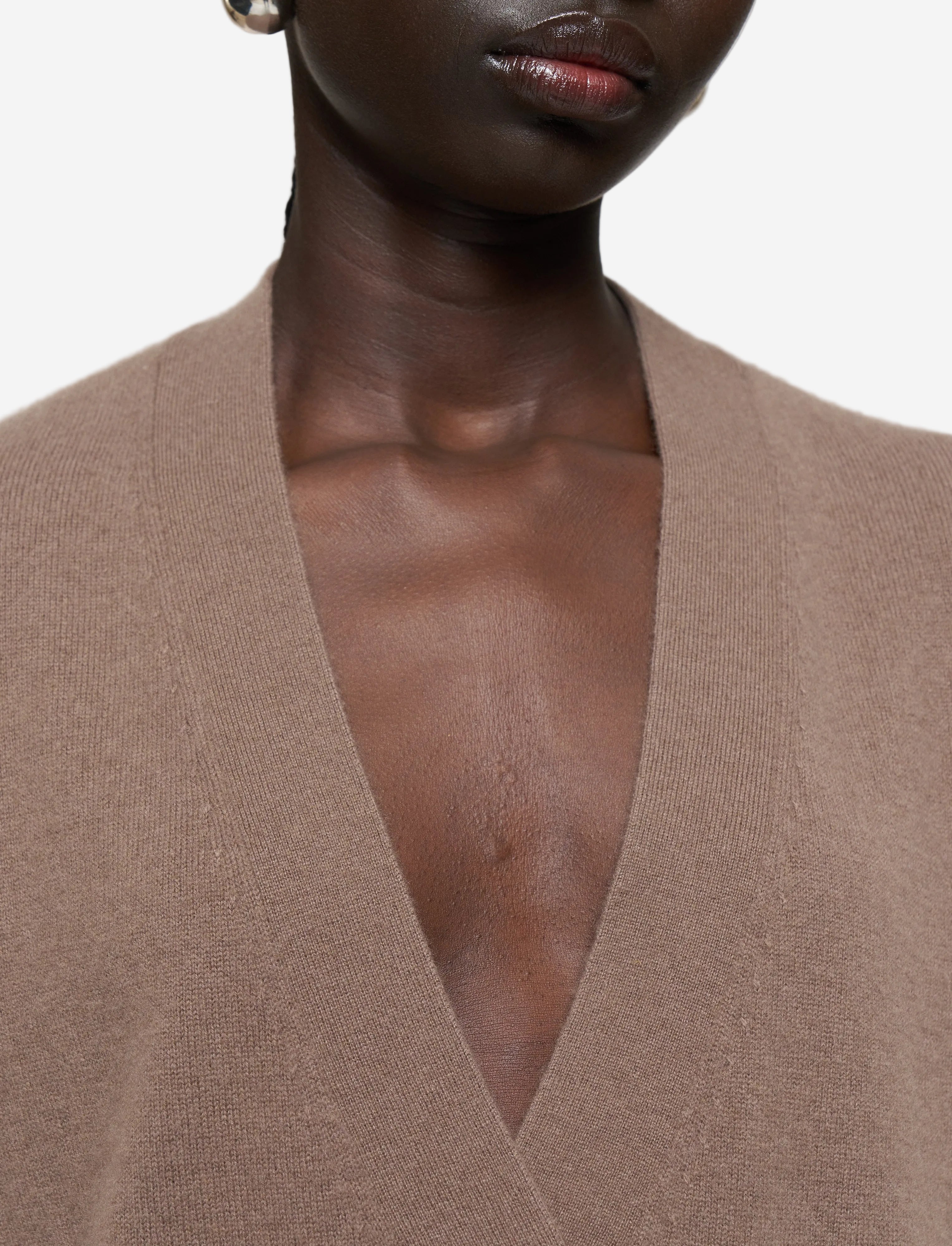 Close-up of a person wearing a brown cardigan against a plain background