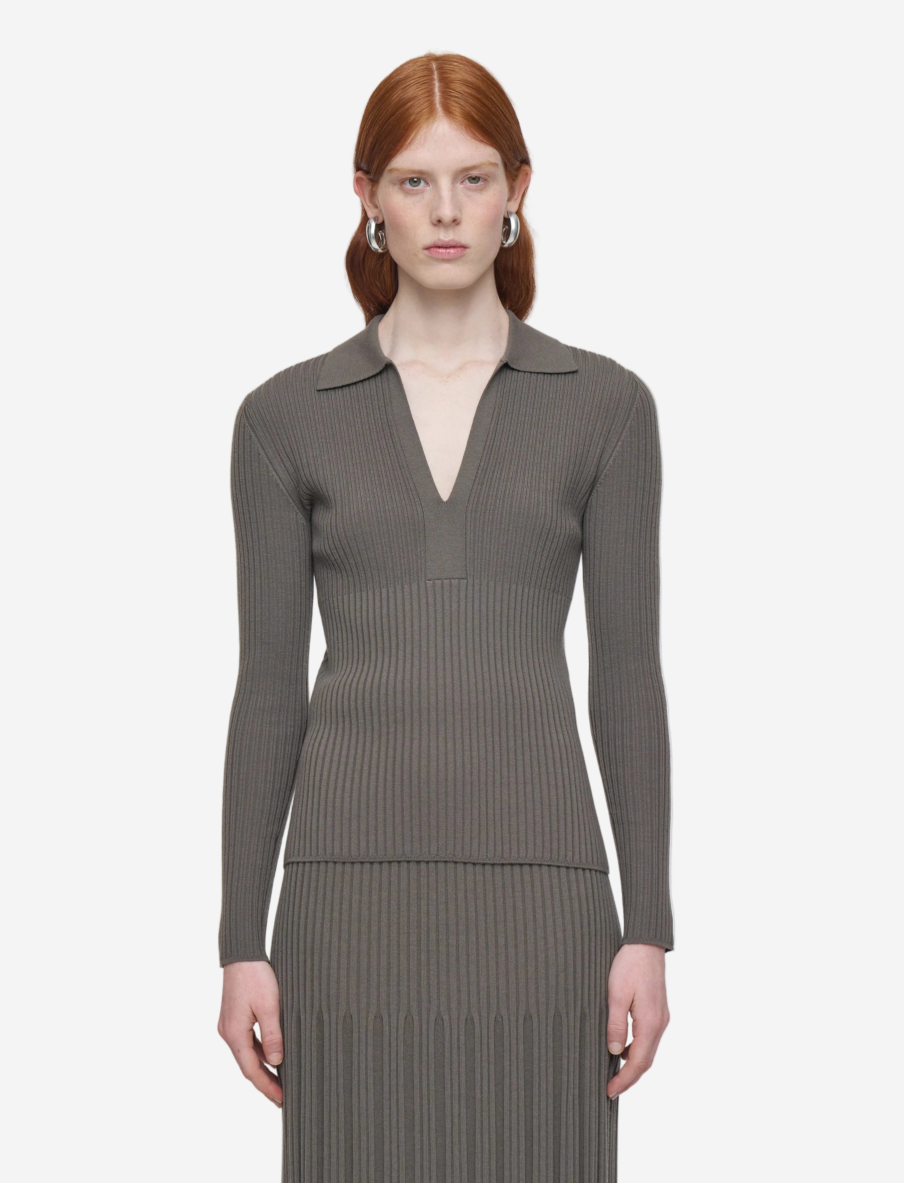 Woman wearing a gray ribbed long-sleeve top and pleated skirt on a white background