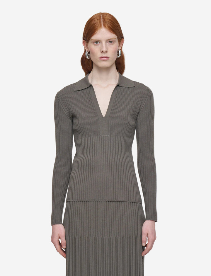 Woman wearing a gray ribbed long-sleeve top and pleated skirt on a white background