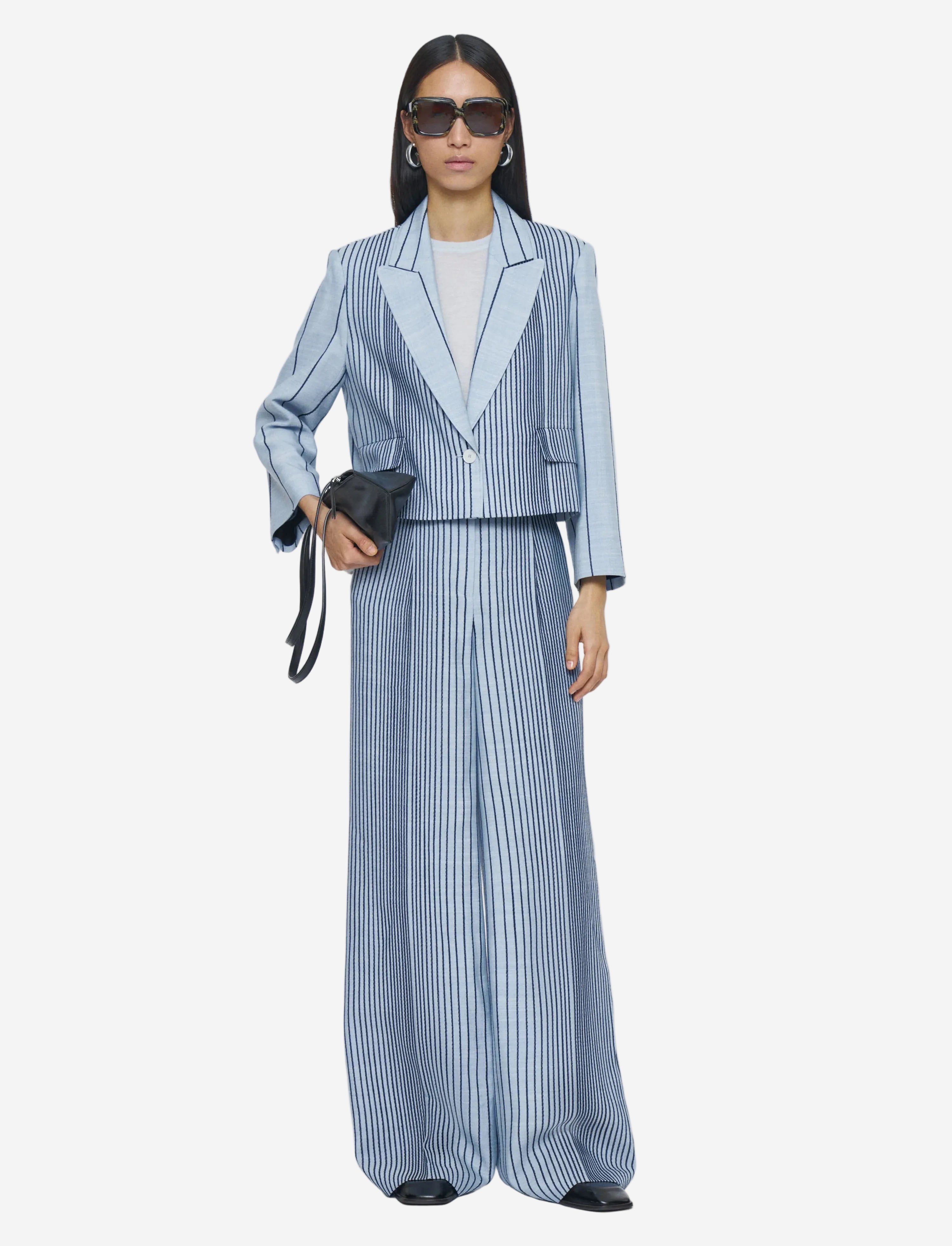 Woman wearing a blue and white striped suit with sunglasses on a light gray background