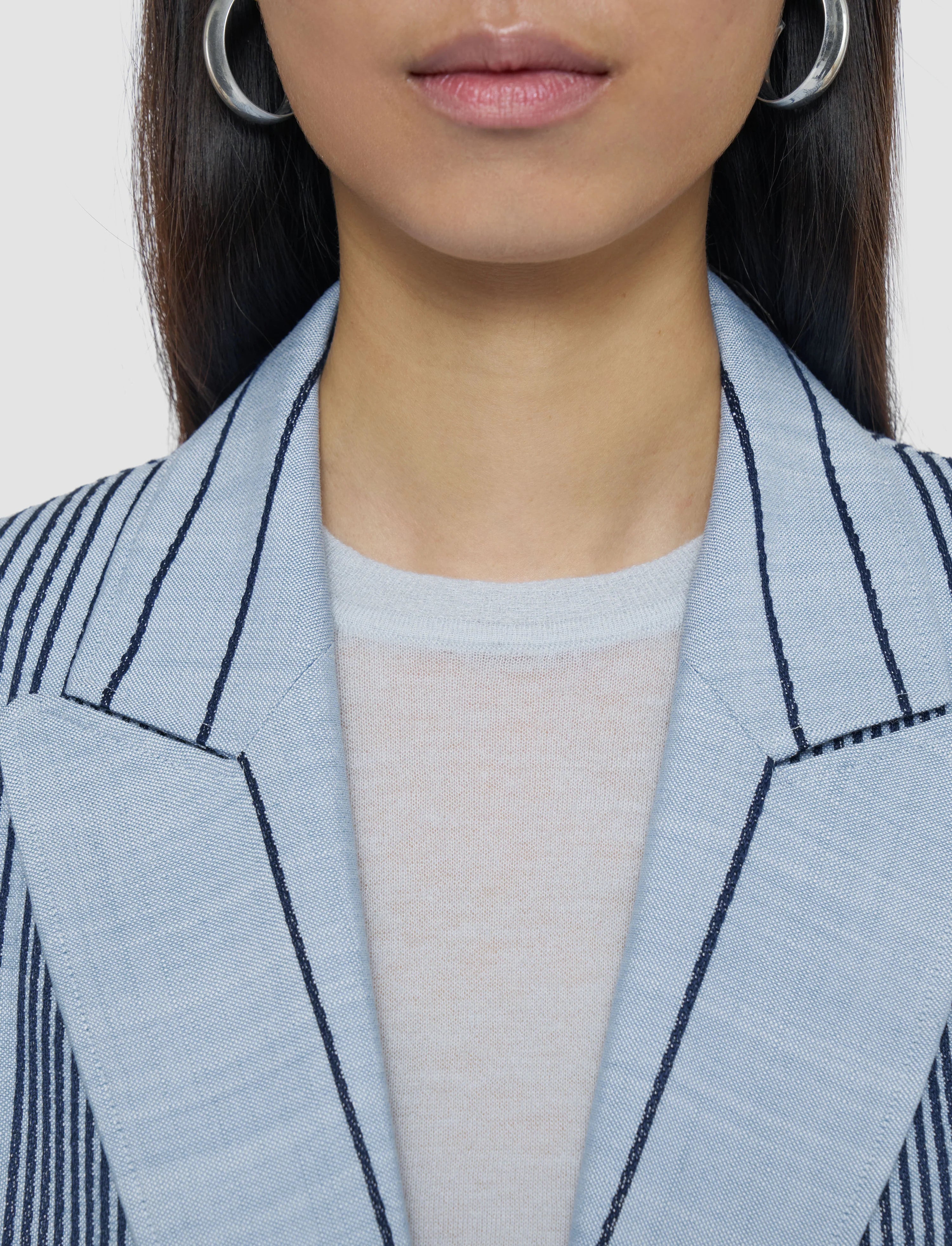Close-up of a person wearing a light blue blazer with black stripes on a plain background