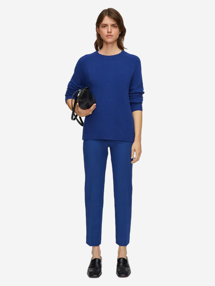 Person wearing a blue sweater and pants holding a black handbag on a white background