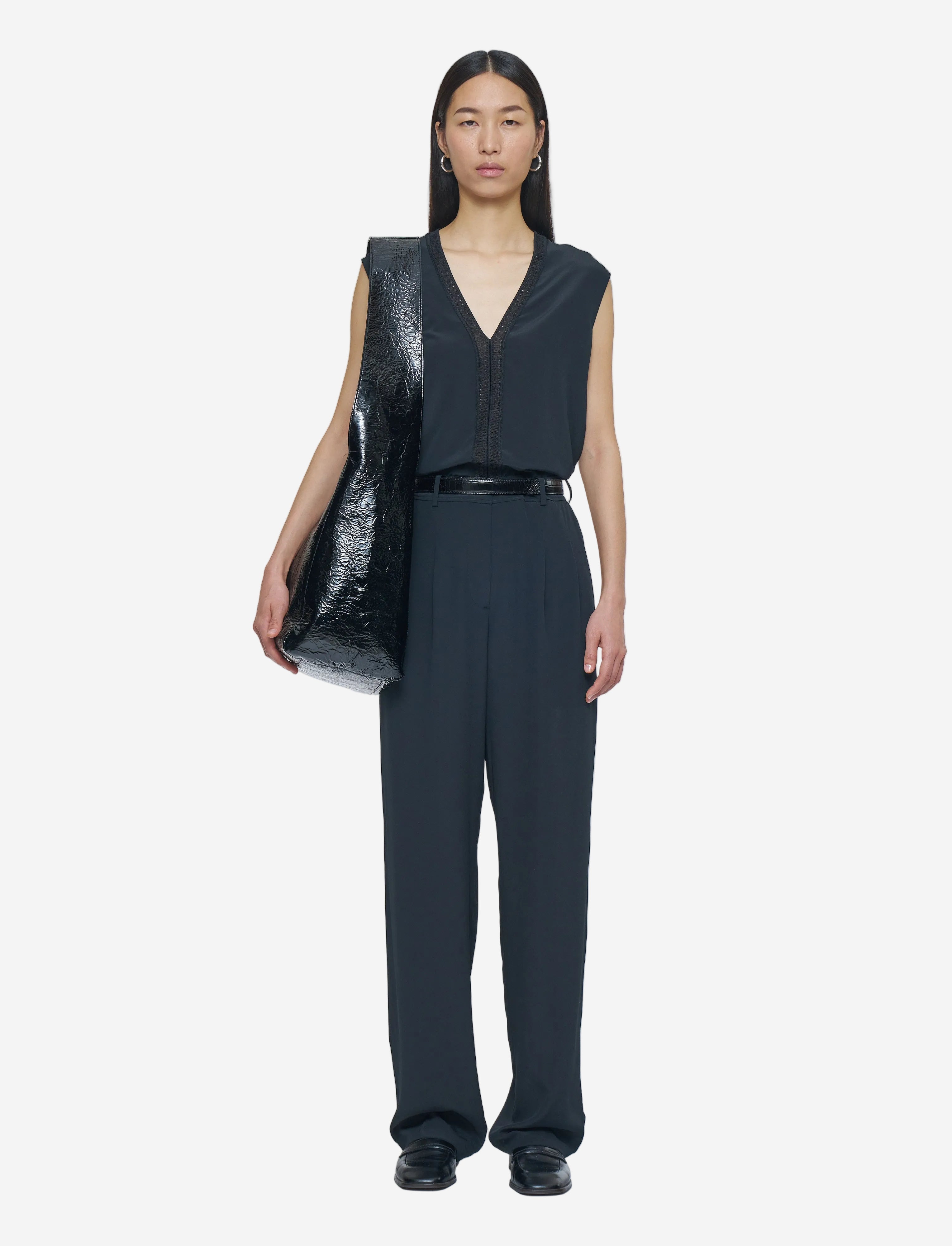 Person wearing a black sleeveless top and pants holding a black vinyl bag on a white background