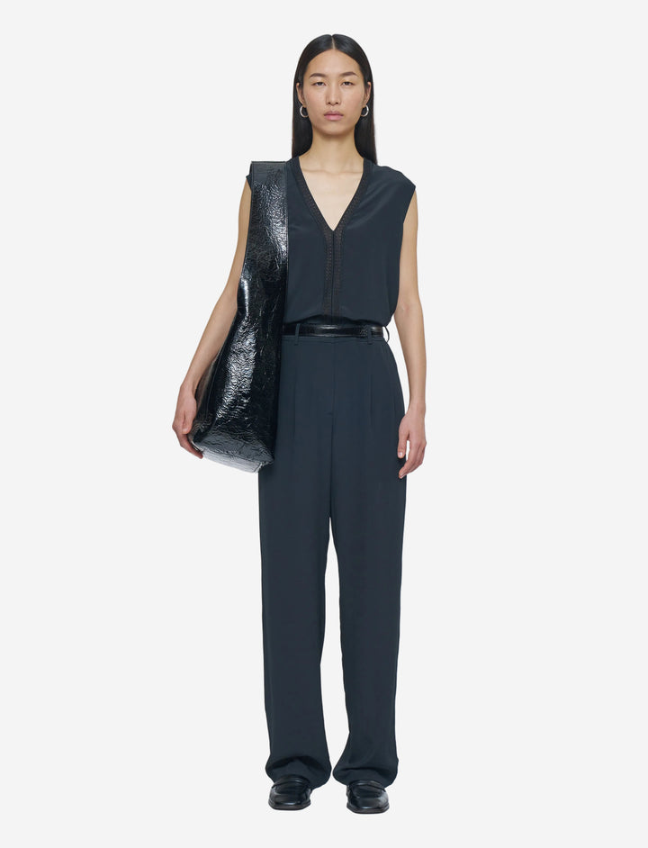 Person wearing a black sleeveless top and pants holding a black vinyl bag on a white background