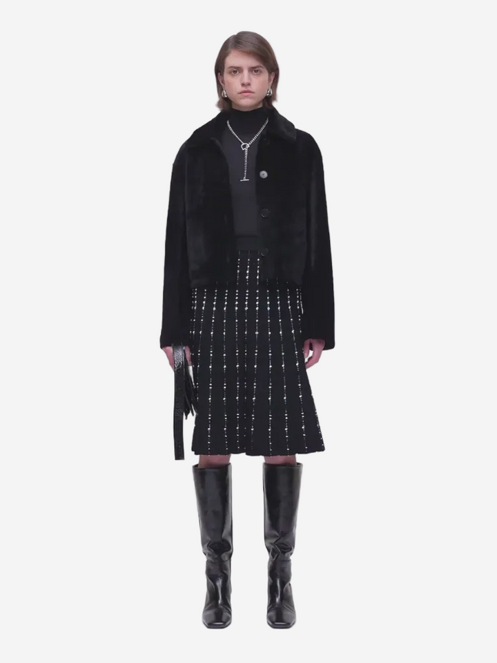 Person wearing a black coat, black top, and black skirt with white pattern on a white background