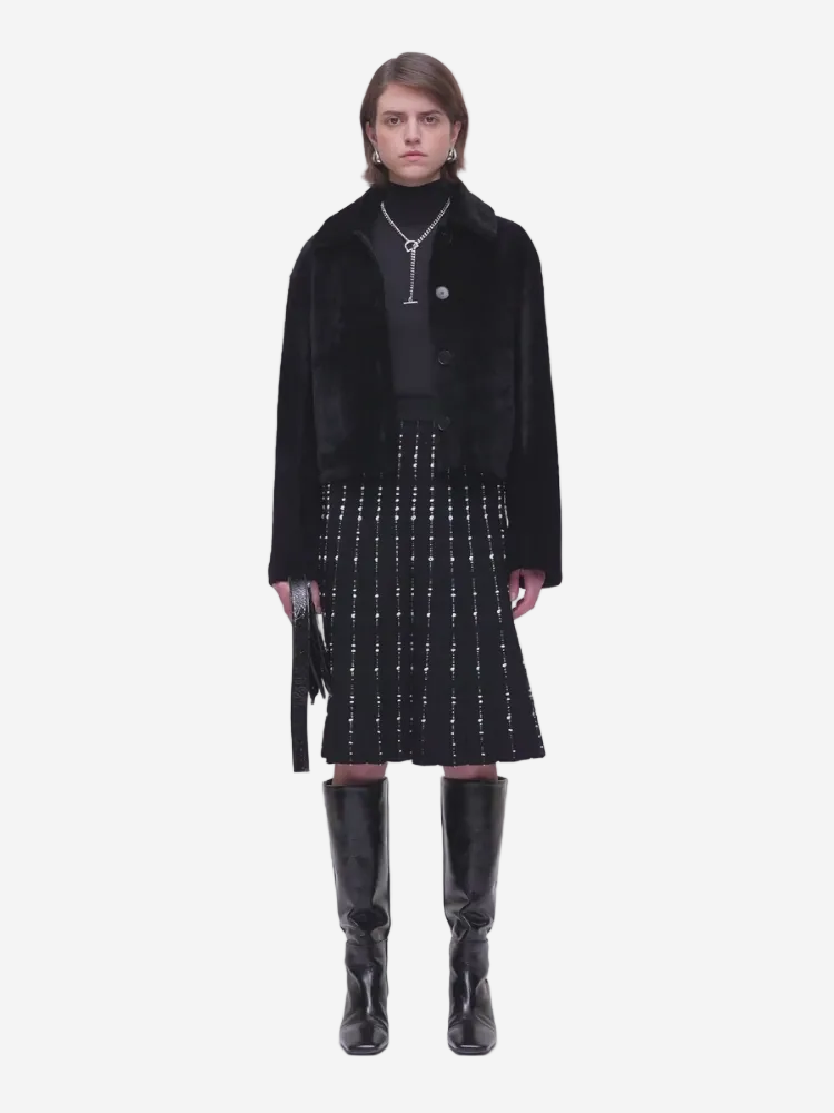 Person wearing a black coat, black top, and black skirt with white pattern on a white background