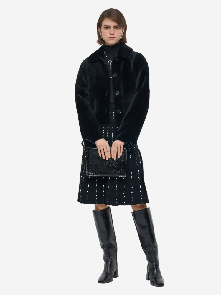 Person wearing a black coat, black dress, and black knee-high boots on a white background