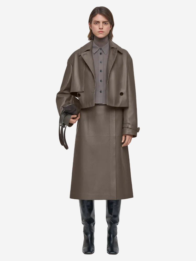 Person wearing a brown leather coat, skirt, and boots on a white background