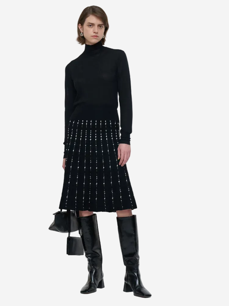 Person wearing a black turtleneck, patterned skirt, and knee-high boots on a white background