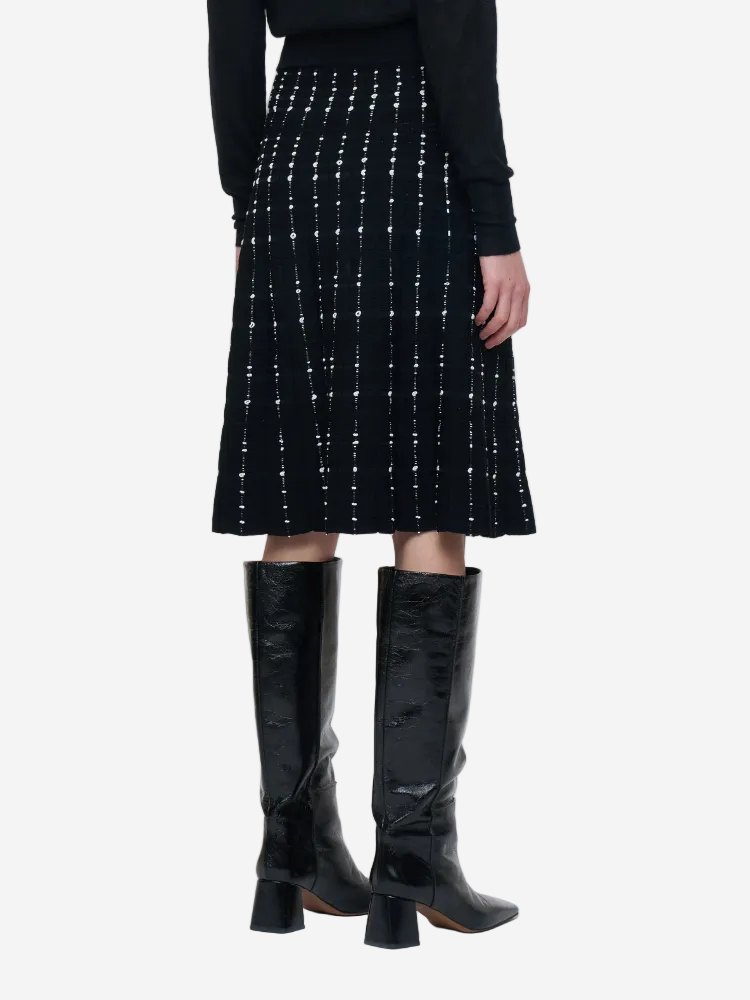 Person wearing a black skirt with white patterns and black knee-high boots on a white background