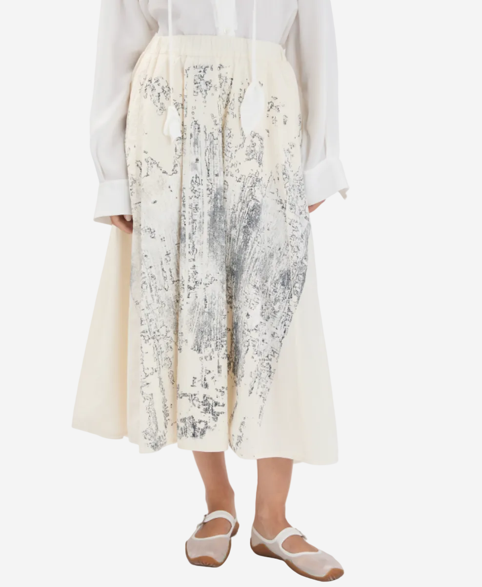 Person wearing a white blouse and a long, light-colored skirt with a subtle pattern on a white background