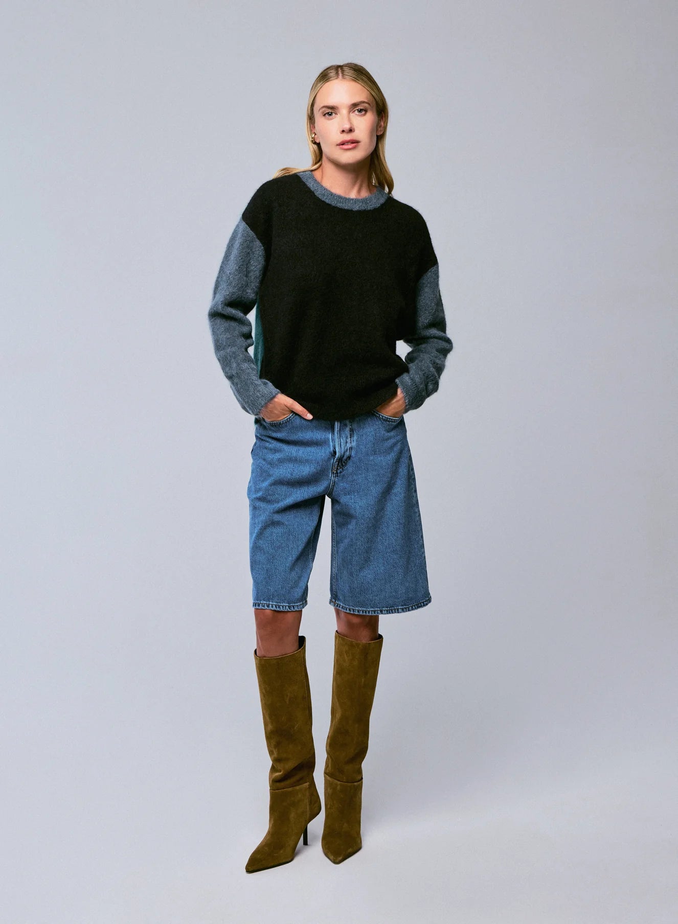 Woman wearing a black and gray sweater with blue jeans and green boots on a white background