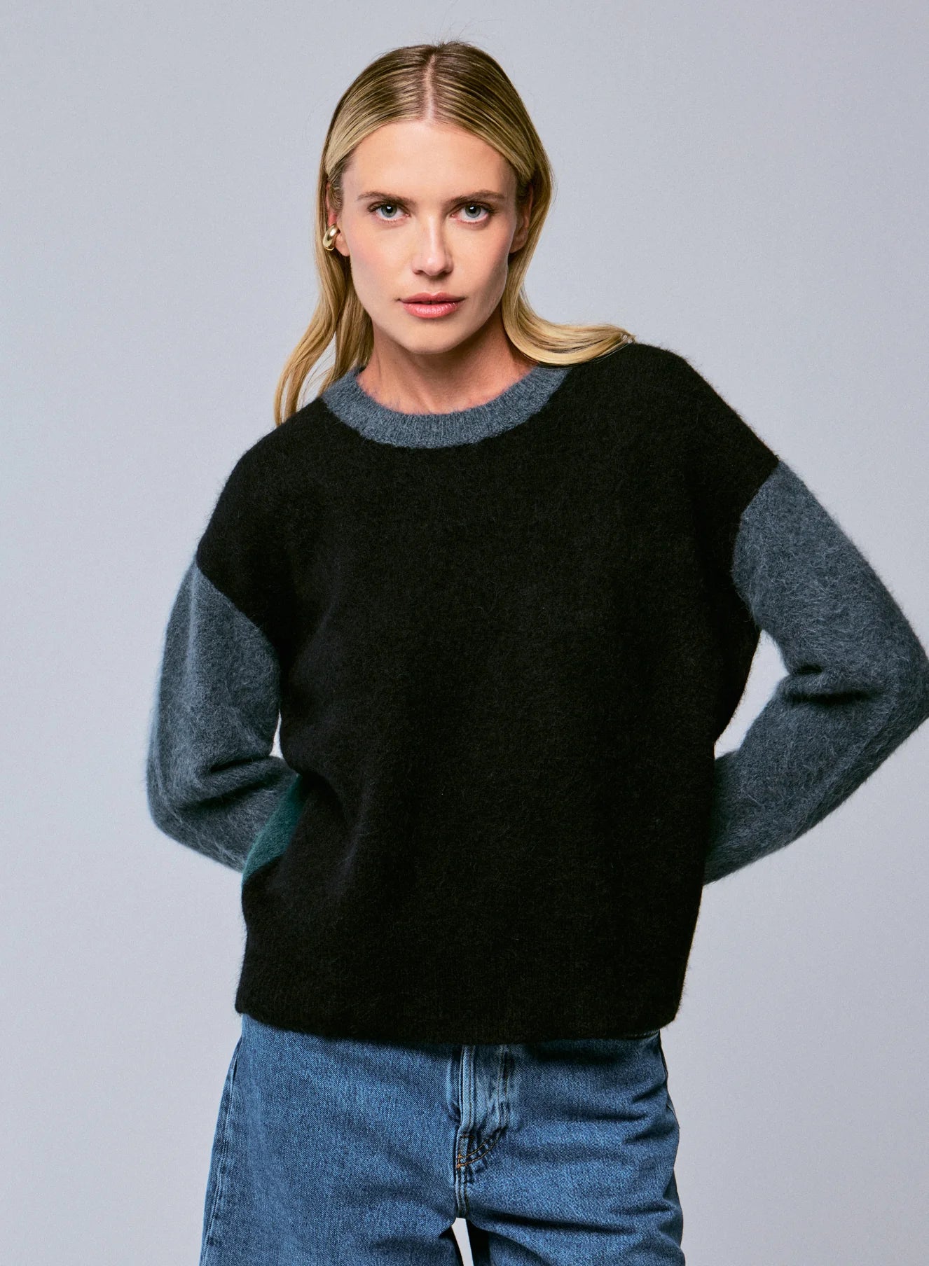 Woman wearing a black sweater with gray sleeves against a gray background