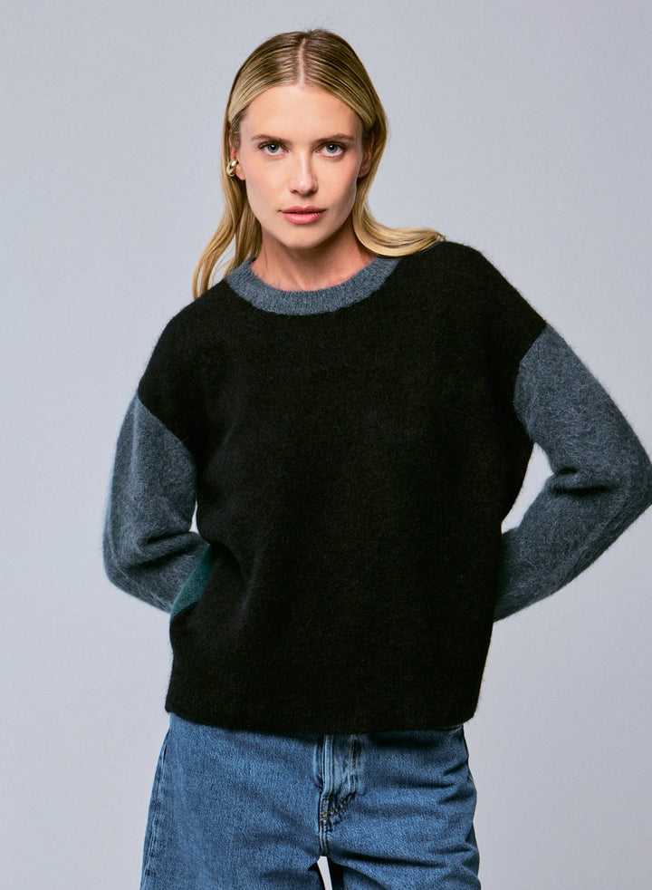 Woman wearing a black sweater with gray sleeves against a gray background