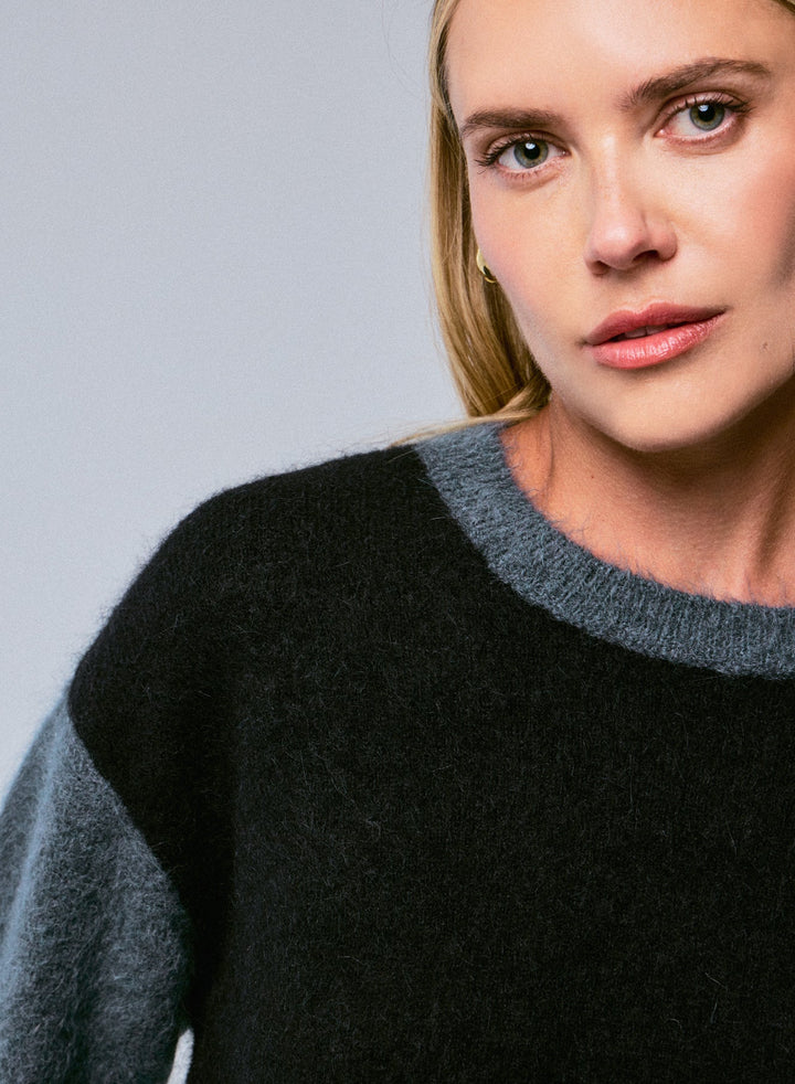Person wearing a black and gray sweater against a plain background
