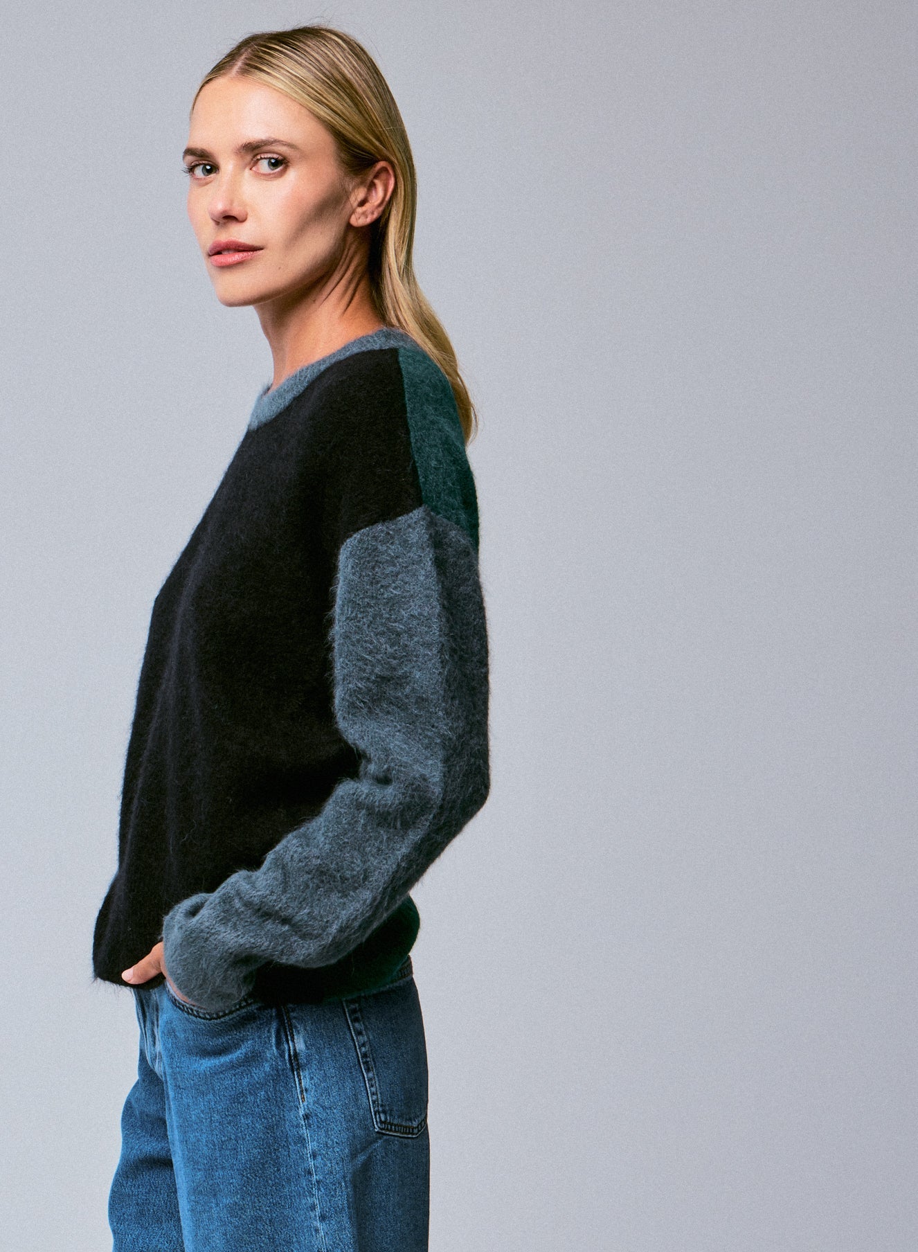 Woman wearing a black and gray sweater with blue jeans on a gray background