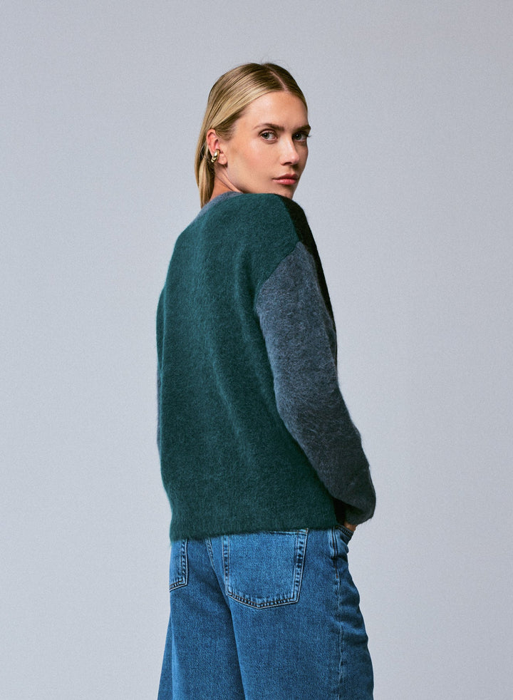 Person wearing a green sweater with gray sleeves against a gray background