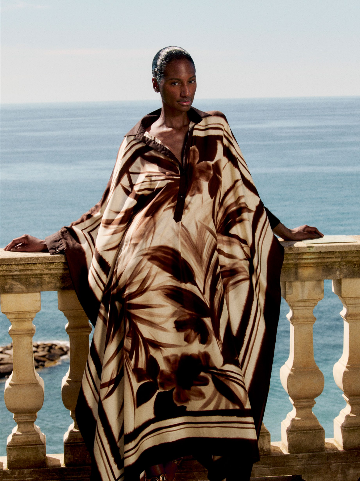 Woman wrapped in a patterned blanket standing on a balcony with ocean view