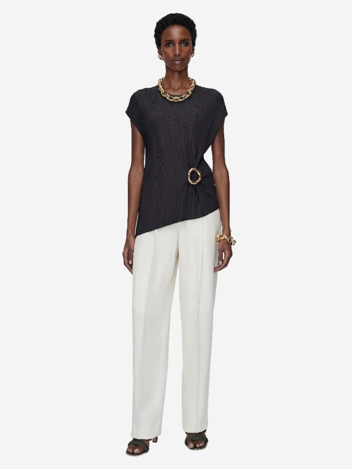 Woman wearing a black top and white pants on a plain background