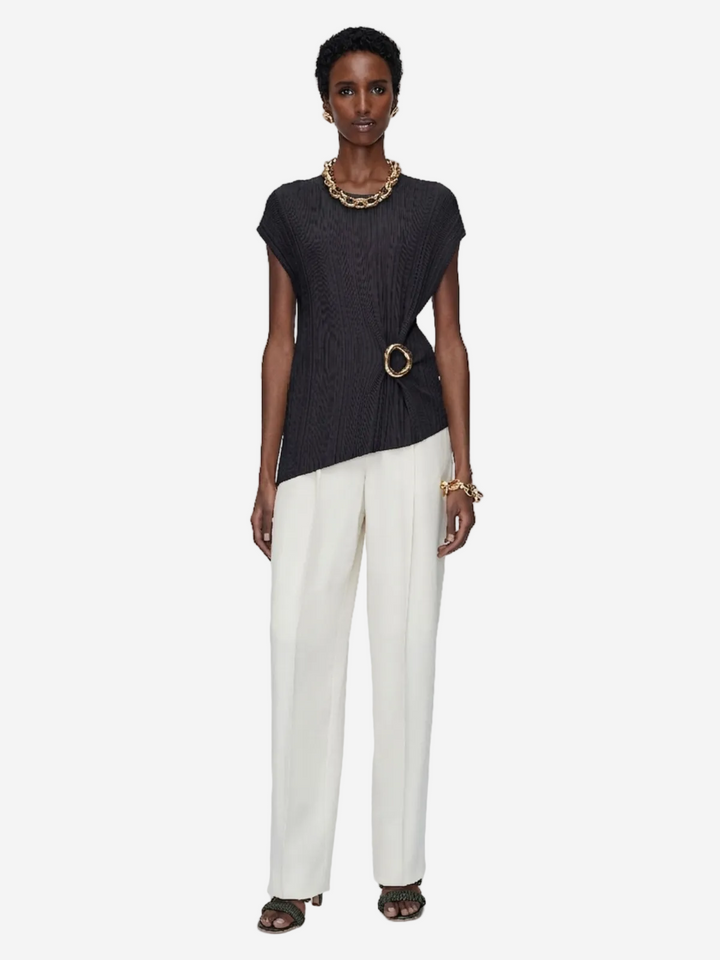 Woman wearing a black top and white pants on a plain background