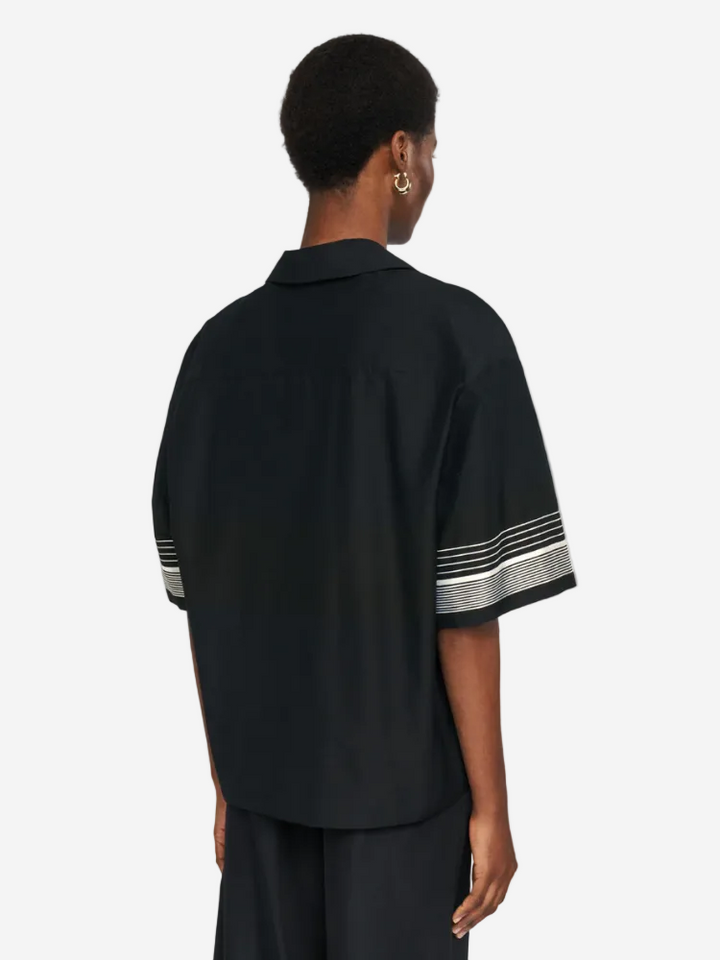 Person wearing a black shirt with white stripes on sleeves against a light gray background