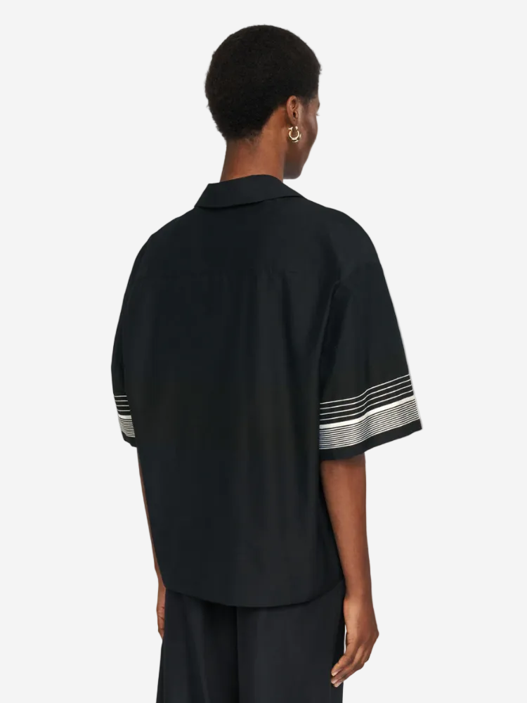 Person wearing a black shirt with white stripes on sleeves against a light gray background
