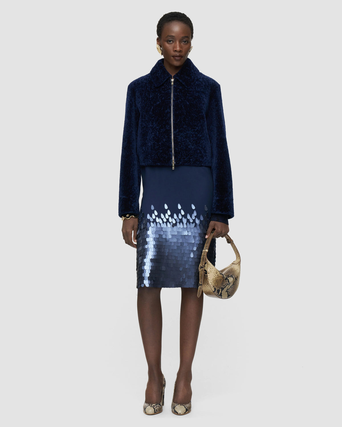 Model wearing the JOSEPH Liris navy shearling jacket over a sequin midi skirt with snakeskin heels and bag