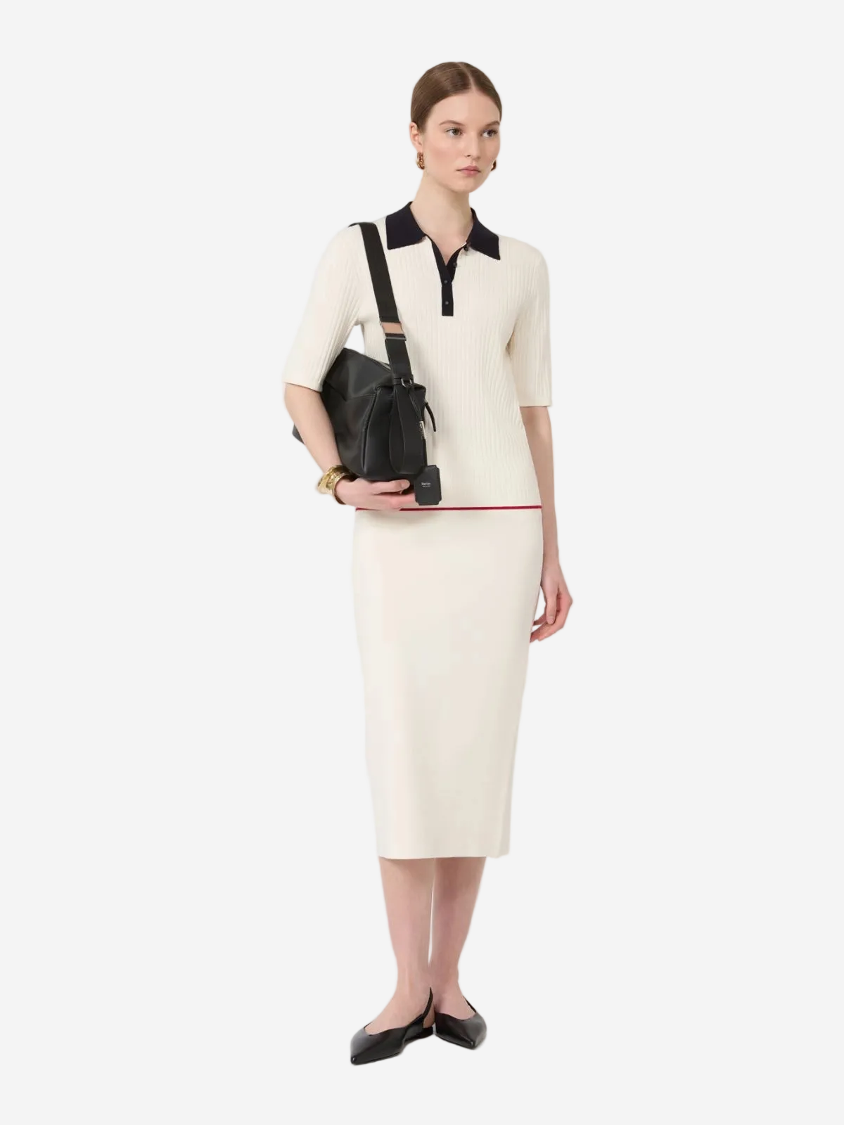 Woman wearing a cream dress with black accents, holding a black handbag on a white background