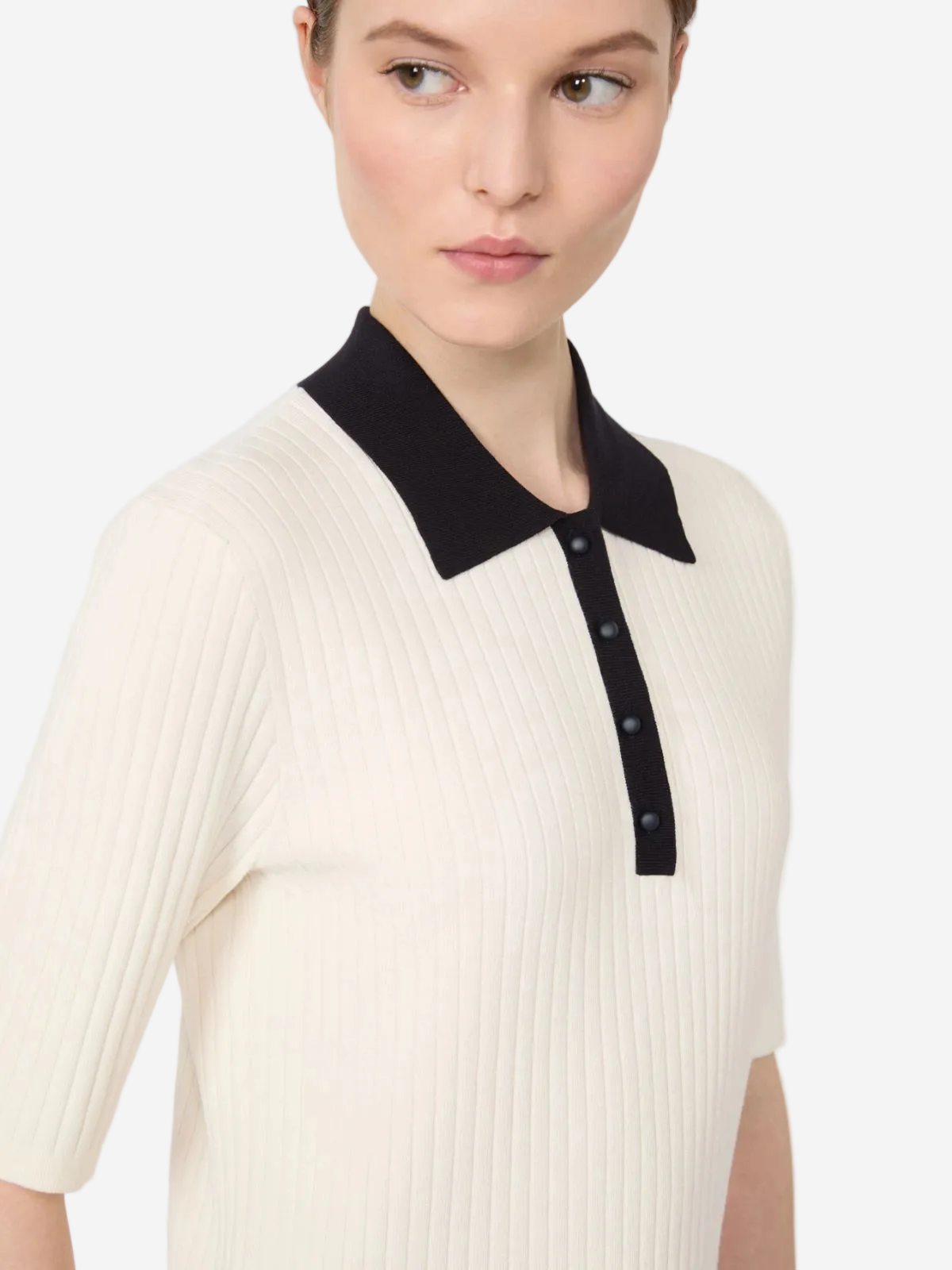 Woman wearing a white ribbed sweater with a black collar on a light gray background